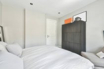 Intérieur de la chambre lumineuse moderne avec lit doux et armoire en bois placée sur le tapis près de la fenêtre avec rideaux et TV dans le coin — Photo de stock
