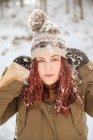 Спокойная женщина со снегом на шляпе и волосами, смотрящая в камеру в зимнем лесу — стоковое фото