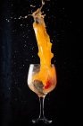 Холодный алкоголь апельсиновый напиток выплескивается из стеклянного кубка на черном фоне в студии — стоковое фото