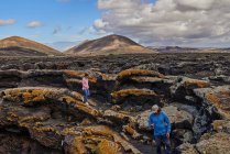 Dall'alto uomo e donna con gli zaini che camminano sul pendio ruvido della montagna contro il cielo blu nuvoloso a Fuerteventura, Spagna — Foto stock