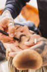 Homem anônimo manchando fundação do rosto da mulher loira durante o trabalho no estúdio de maquiagem profissional — Fotografia de Stock