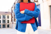 Cropped unrecognizable female freelancer with netbook in red case standing in city street and looking forward — Stock Photo