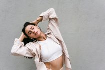 Carefree female dancer listening to music in earphones and dancing with closed eyes while enjoying songs on background of gray wall in city — Stock Photo