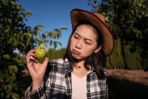Sad ethnic female farmer standing with ripe pear bitten by insects in garden in village — Stock Photo
