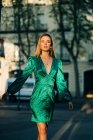 Donna spensierata in abito verde alla moda in piedi con le braccia tese in strada e guardando la fotocamera — Foto stock
