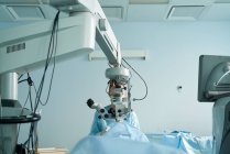 Внимательная женщина-врач в хирургической форме и стерильной маске смотрит через микроскоп во время операции глаза неузнаваемого пациента в больнице — стоковое фото