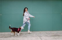 Vista laterale del proprietario femminile che corre con il cane Border Collie al guinzaglio mentre si diverte durante una passeggiata in città — Foto stock