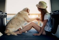 Barefoot woman holding paw of loyal Golden Retriever dog while sitting on bed inside RV during road trip in nature — Stock Photo