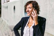 Positive erwachsene weibliche Führungskraft in edlem Outfit, die mit der Hand auf der Taille steht und an sonnigen Tagen mit dem Handy telefoniert — Stockfoto