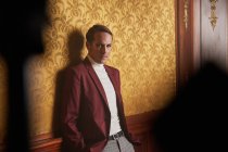 Confident adult male actor in elegant classy clothes keeping hand in pocket and looking away thoughtfully while standing near wall in vintage style room — Stock Photo