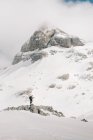 Vista lateral del atleta anónimo sobre esquís en Pico Aunamend en los Pirineos nevados Montañas bajo el cielo nublado en Navarra España - foto de stock