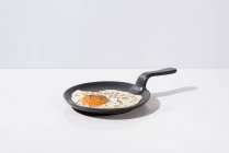 Смачне смажене яйце на чорній сковороді, що подається на столі на білому тлі в студії — стокове фото