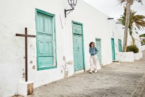 Seitenansicht einer Frau mit Rucksack, die auf dem Bürgersteig vor weißen Häusern und wolkenverhangenem grauen Himmel auf der Stadtstraße in Fuerteventura, Spanien läuft — Stockfoto