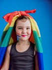 Bambina con legato bandiera arcobaleno sulla testa guardando la fotocamera mentre in piedi sullo sfondo blu — Foto stock