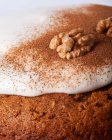 Nahaufnahme von leckerem Möhrenkuchenstück mit Walnuss- und Zimtpulver auf Puderzuckerglasur auf hellem Hintergrund — Stockfoto