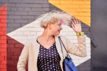Alternativa spensierata femminile gettare i capelli corti tinti contro muro colorato in zona urbana — Foto stock