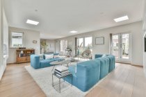 Innengestaltung des offenen Wohnbereichs mit blauem Sofa und Stühlen in der Nähe eines kleinen Tisches auf weichem Teppich in einer modernen Wohnung mit weißen Wänden und lampenbeleuchteter Decke — Stockfoto