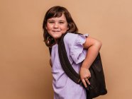 Cute schoolchild standing on brown background in studio and looking at camera — Stock Photo