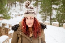 Жінка зі снігом на капелюсі і волоссям дивиться на камеру в зимовому лісі — стокове фото