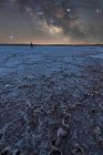 Silhouette of explorer standing in dry salt lagoon on background of starry sky with glowing Milky Way at night — Stock Photo
