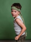 Alegre niño de karate preadolescente en hachimaki pañuelo de cabeza de pie sobre fondo verde en el estudio y divertirse - foto de stock