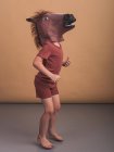 Посторонний вид анонимного ребенка в маске лошади, представляющего концепцию скачущего жеребца на бежевом фоне — стоковое фото