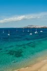 Praia com veleiros ao fundo em um mar azul-turquesa sob um céu com nuvens no dia ensolarado de verão em Fuerteventura, Espanha — Fotografia de Stock