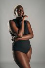 Afro-americano curvy feminino no preto bodysuit de pé com a mão sobre o rosto no cinza fundo no estúdio — Fotografia de Stock