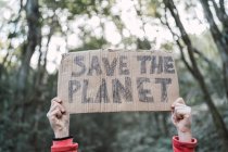 Cropped unrecognizable ethnic child showing Save The Planet title on carton piece while looking at camera in forest — Stock Photo