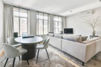 Design de interiores elegante casa com confortáveis cadeiras macias colocadas em torno da mesa oval com vaso decorativo na sala de estar moderna — Fotografia de Stock