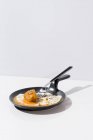 Металева виделка зі свіжим шматком хліба, зануреним у рідкий жовток смаженого яйця, що подається на сковороді на білому тлі — стокове фото