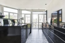 Modernes Wohndesign mit geräumiger offener Küche mit schwarzen Möbeln und Zierfliesen am Boden und großen Panoramafenstern mit Blick auf städtische Gebäude — Stockfoto
