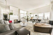 Інтер'єр сучасної просторої вітальні зі зручним диваном і дерев'яним столом і стільцями в сучасній розкішній квартирі з панорамними вікнами — стокове фото
