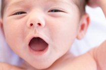 From above adorable naked in infant yawning sweetly while lying on soft bed at home — Stock Photo