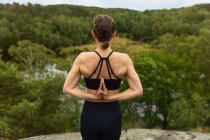 Mujer delgada irreconocible agarrándose de las manos detrás de la espalda mientras practica yoga en la naturaleza en verano - foto de stock