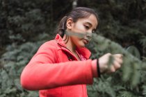 Bambino etnico focalizzato con foglia di pianta verde che guarda attraverso la lente d'ingrandimento nei boschi esplorando la foresta durante il giorno — Foto stock