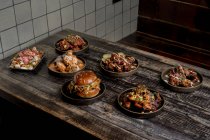 Сверху аппетитные куриные крылышки в соусе барбекю помещены рядом с гамбургером и картошкой фри на деревянном столе в ресторане — стоковое фото