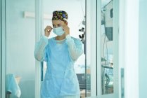 Medico donna adulto in uniforme chirurgica e cappuccio medico ornamentale indossando maschera monouso mentre in attesa in ospedale — Foto stock
