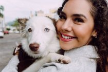 Encantada propietaria femenina abrazando al lindo perro Border Collie y sonriendo con los ojos cerrados - foto de stock