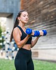 Deportista femenina determinada haciendo ejercicio con pesas durante el entrenamiento de fitness en la calle de la ciudad en verano - foto de stock