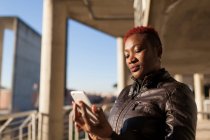Vista laterale della bella donna afro che comunica con il suo smartphone — Foto stock