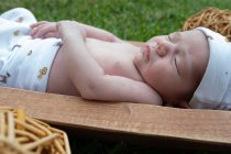 Bonito bebê recém-nascido pequeno dormindo enquanto deitado na banheira de madeira colocada na grama verde — Fotografia de Stock