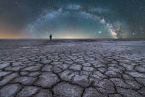 Silueta distante del explorador de pie y sosteniendo una linterna en la laguna de sal seca en el fondo del cielo estrellado con la Vía Láctea brillante en la noche - foto de stock