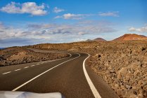 Strada asfaltata dritta che attraversa il campo verso la montagna in mattinata a Fuerteventura, Spagna — Foto stock