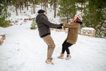 Восхитительная пара в теплой одежде, держась за руки и кружась в снежных зимних лесах, веселясь — стоковое фото
