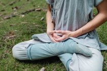 Cropped unrecognizable bald man in traditional clothes sitting on grass in Lotus pose and meditating during kung fu training in forest — Stock Photo