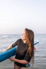 Femme en maillot de bain debout avec SUP board dans l'eau de mer en été et regardant ailleurs — Photo de stock