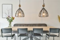 Elegante design interno della moderna sala da pranzo con sedie e divano posizionato vicino al tavolo in legno con mazzo di fiori sotto lampade incandescenti con elementi in metallo in stile loft appartamento — Foto stock