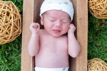 Vista superior de lindo bebé recién nacido durmiendo mientras está acostado en una bañera de madera colocada sobre hierba verde - foto de stock