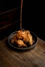 De arriba de la salsa sabrosa que vierte sobre el pollo crujiente puesto en el plato redondo a la mesa de madera en el restaurante - foto de stock
